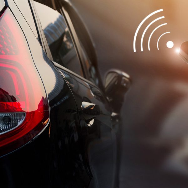 A person holds a remote control, ready to activate the car alarm, standing beside a parked vehicle.