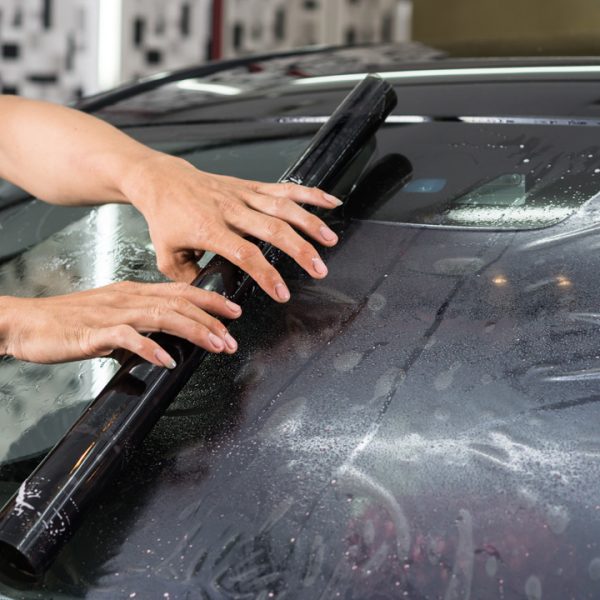 A man cleans the windshield of a car, emphasizing the significance of clear visibility and proper window tinting maintenance.